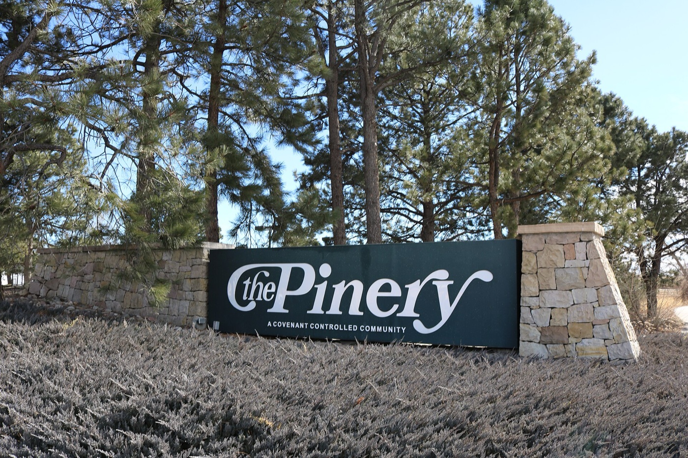 Stone entrance sign for The Pinery community framed by ponderosa pines