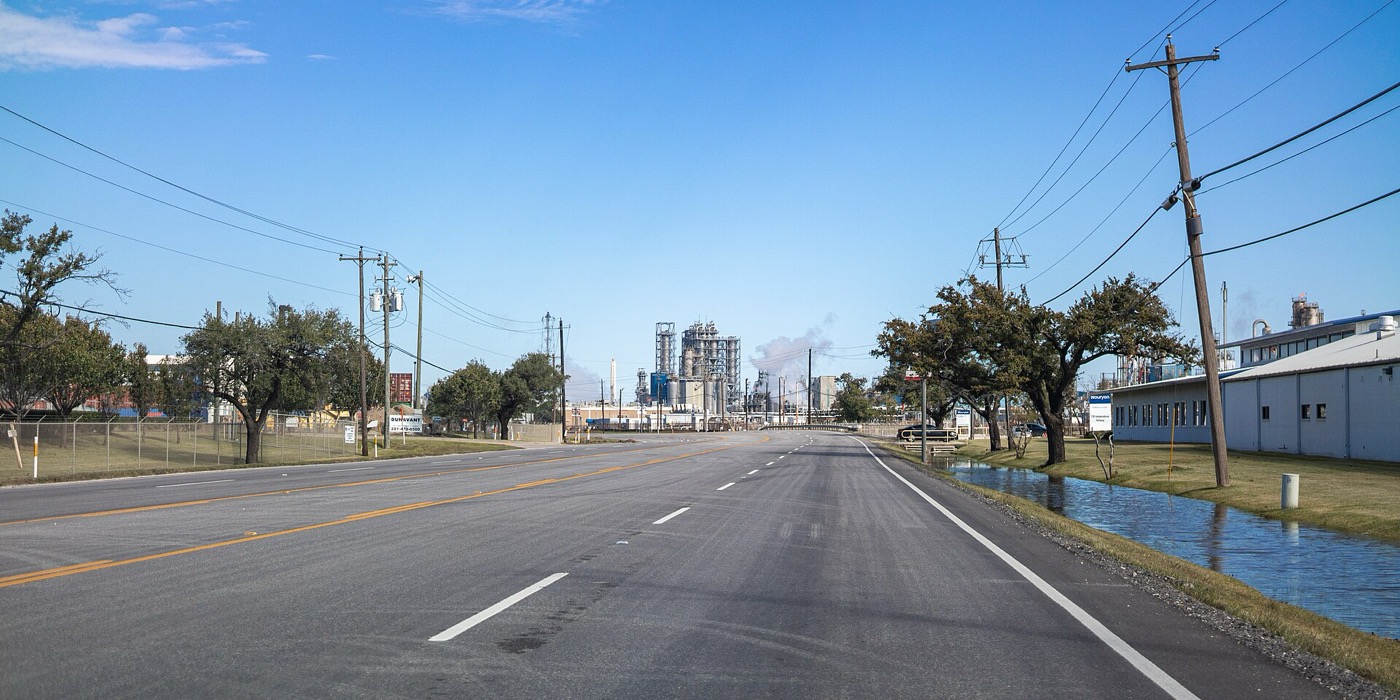 Independence Parkway in Deer Park, Texas, with trees, utility poles and an industrial plant on the horizon
