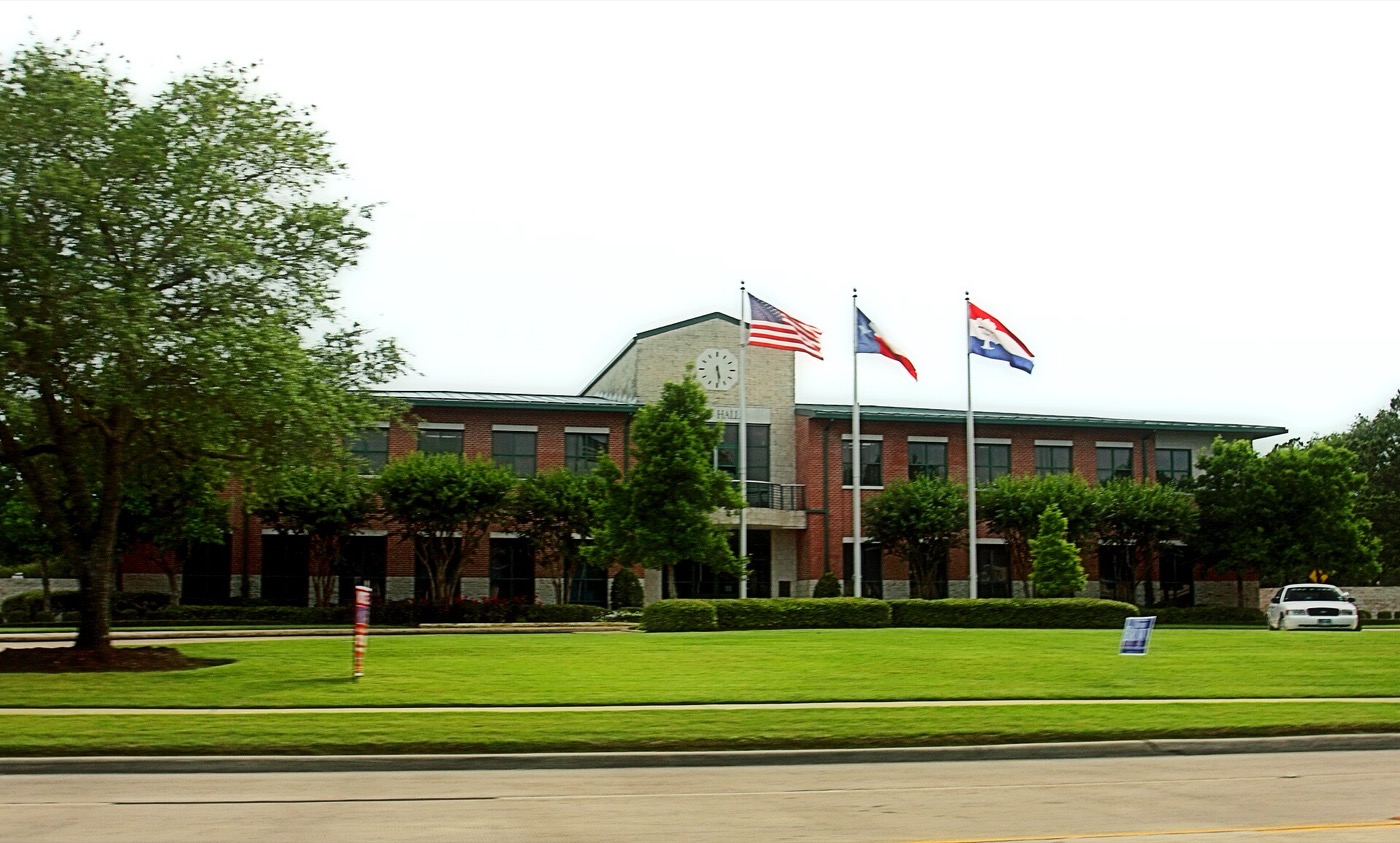 Friendswood City Hall, a two-story brick building with flags on a green lawn