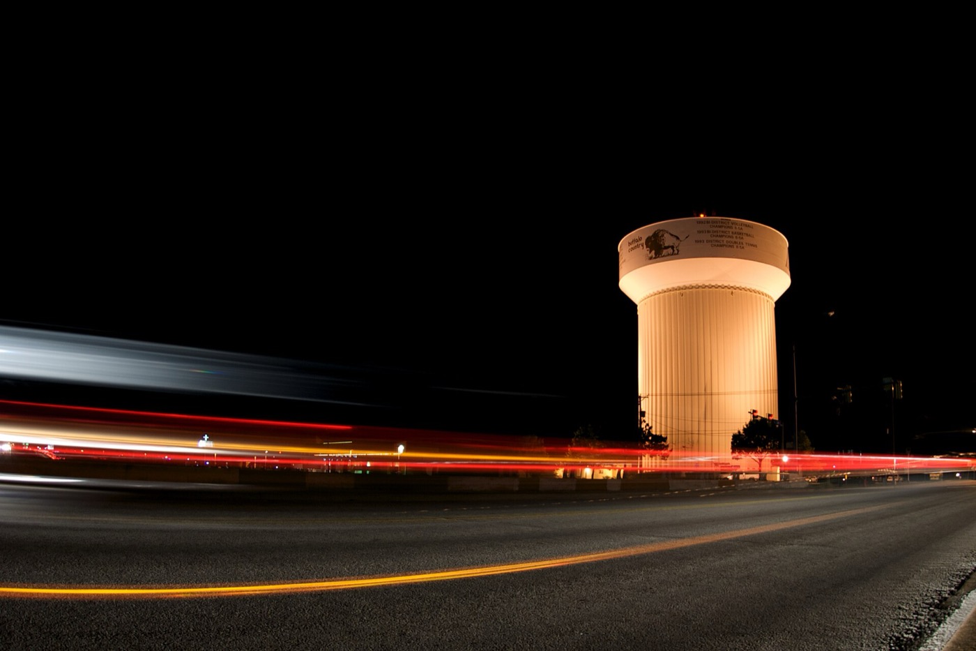 Haltom City water tower lit at night with light trails from traffic on Haltom Road