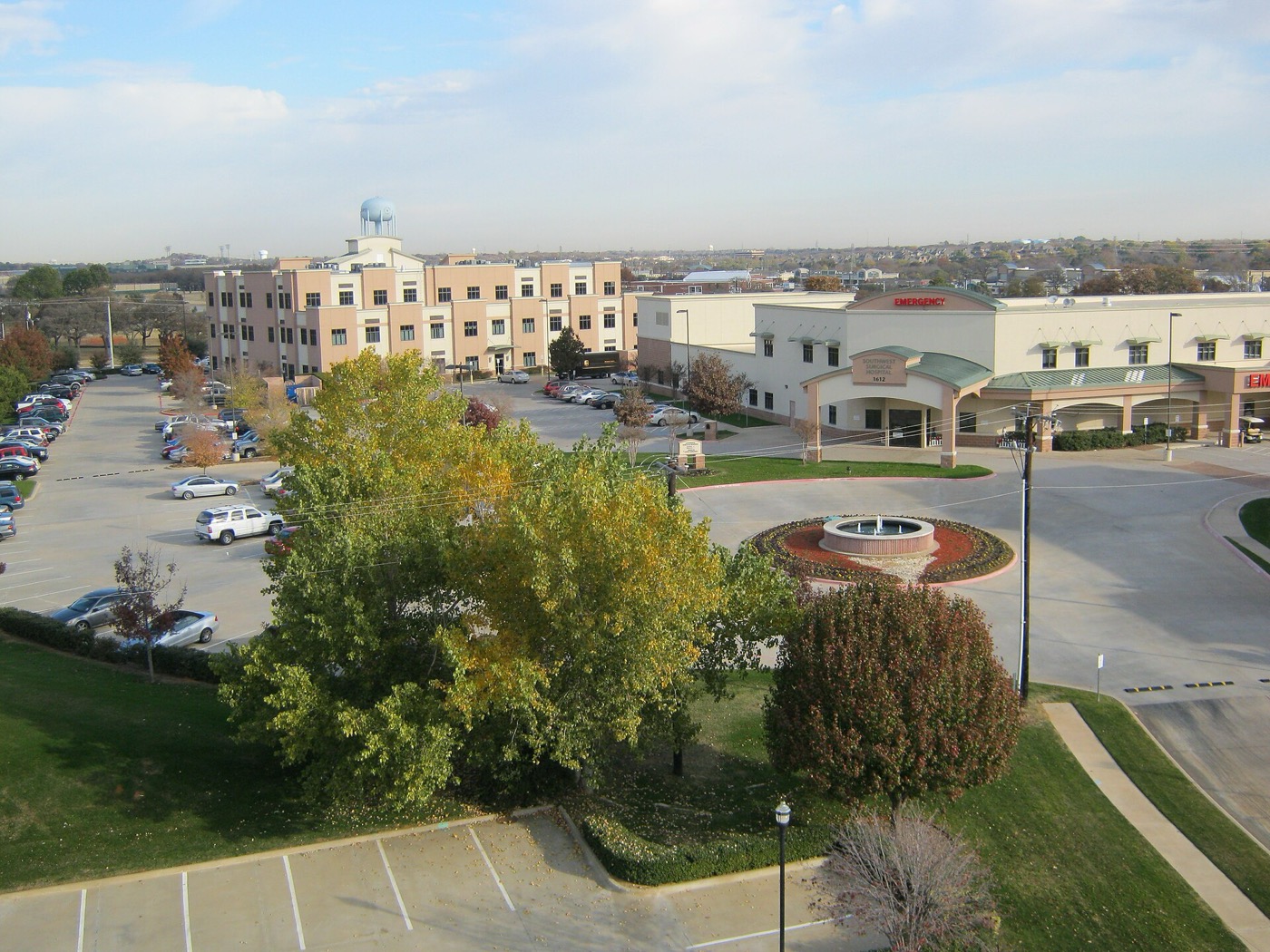 Aerial view over Hurst Town Center with trees, a roundabout fountain and mid-rise buildings in Hurst, Texas