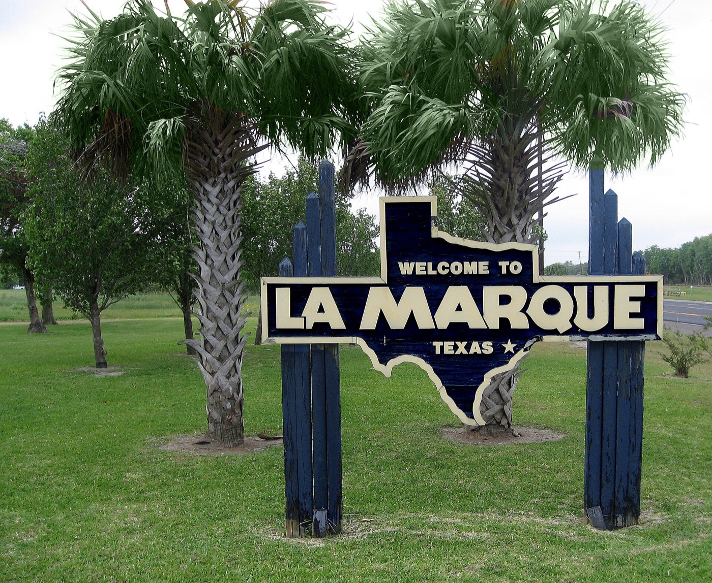 Blue Texas-shaped 'Welcome to La Marque' sign between palm trees