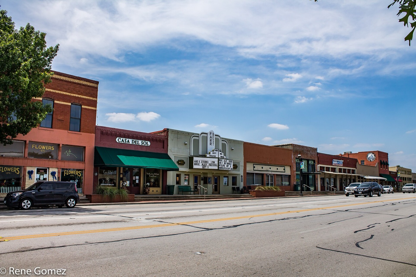 Row of brick and stucco storefronts along a street in downtown Mansfield on a sunny day