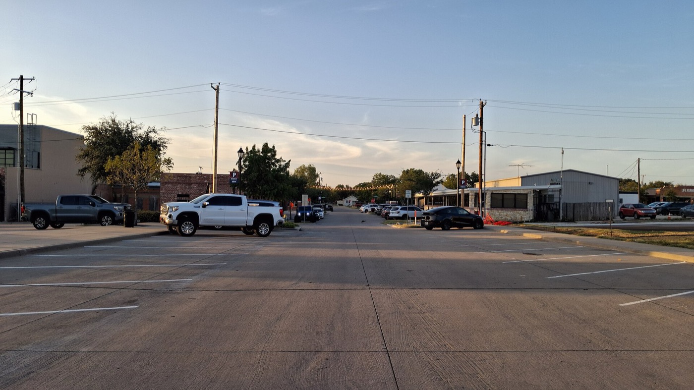 Wide Main Street with parked pickup trucks and low commercial buildings in downtown Prosper, Texas
