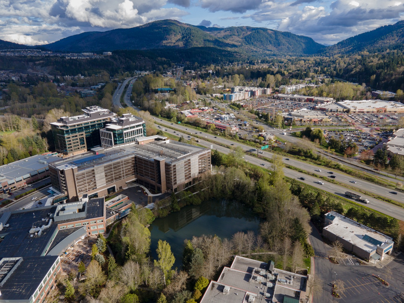 Drone view over Issaquah, Washington, with office buildings, a pond, Interstate 90 and forested foothills