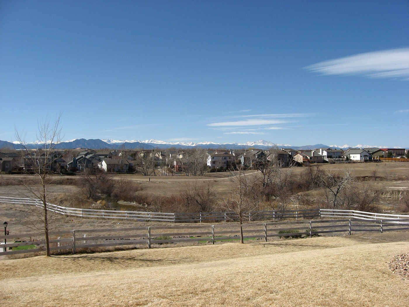 Open space and fence in front of a row of Westminster houses with the Rocky Mountains in the distance