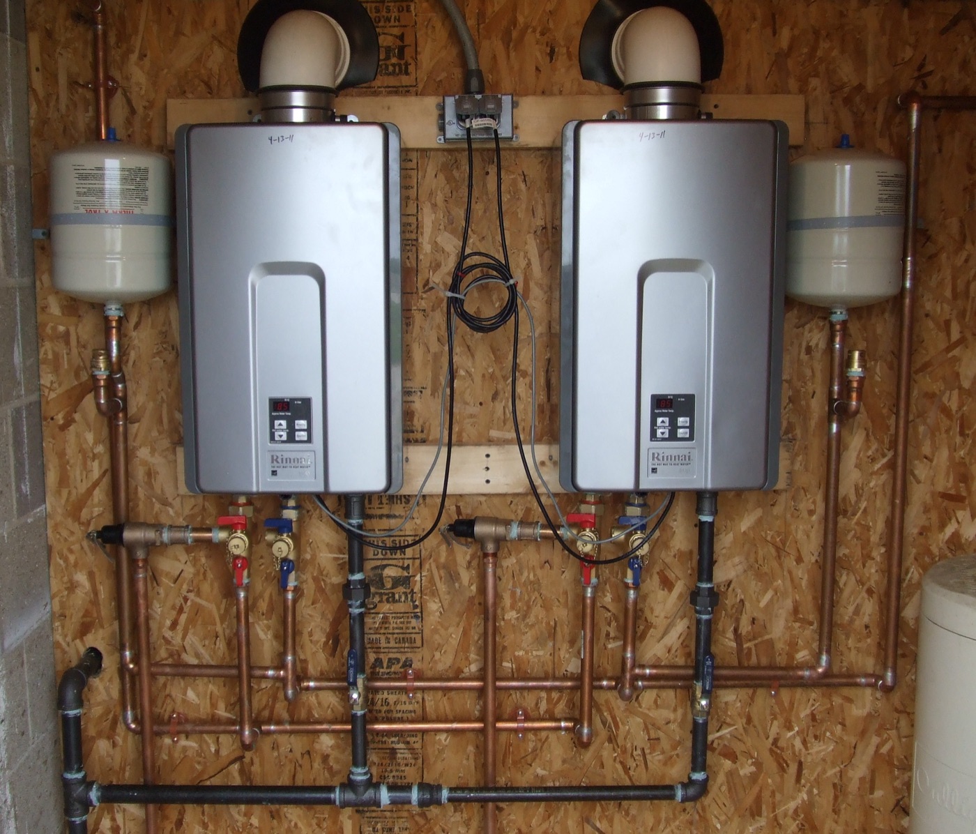 Two real wall-mounted Rinnai tankless water heaters with visible pipes and vents